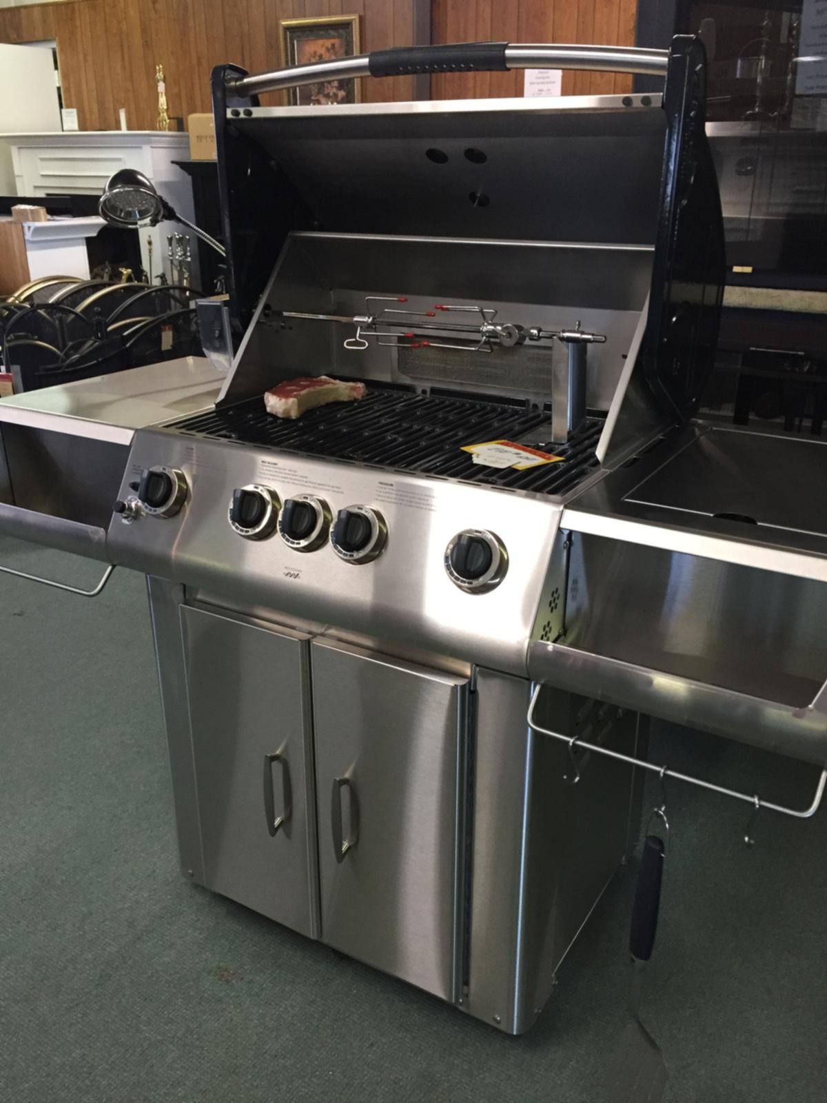 A stainless gas grill on a rolling cart with the lid open in our showroom
