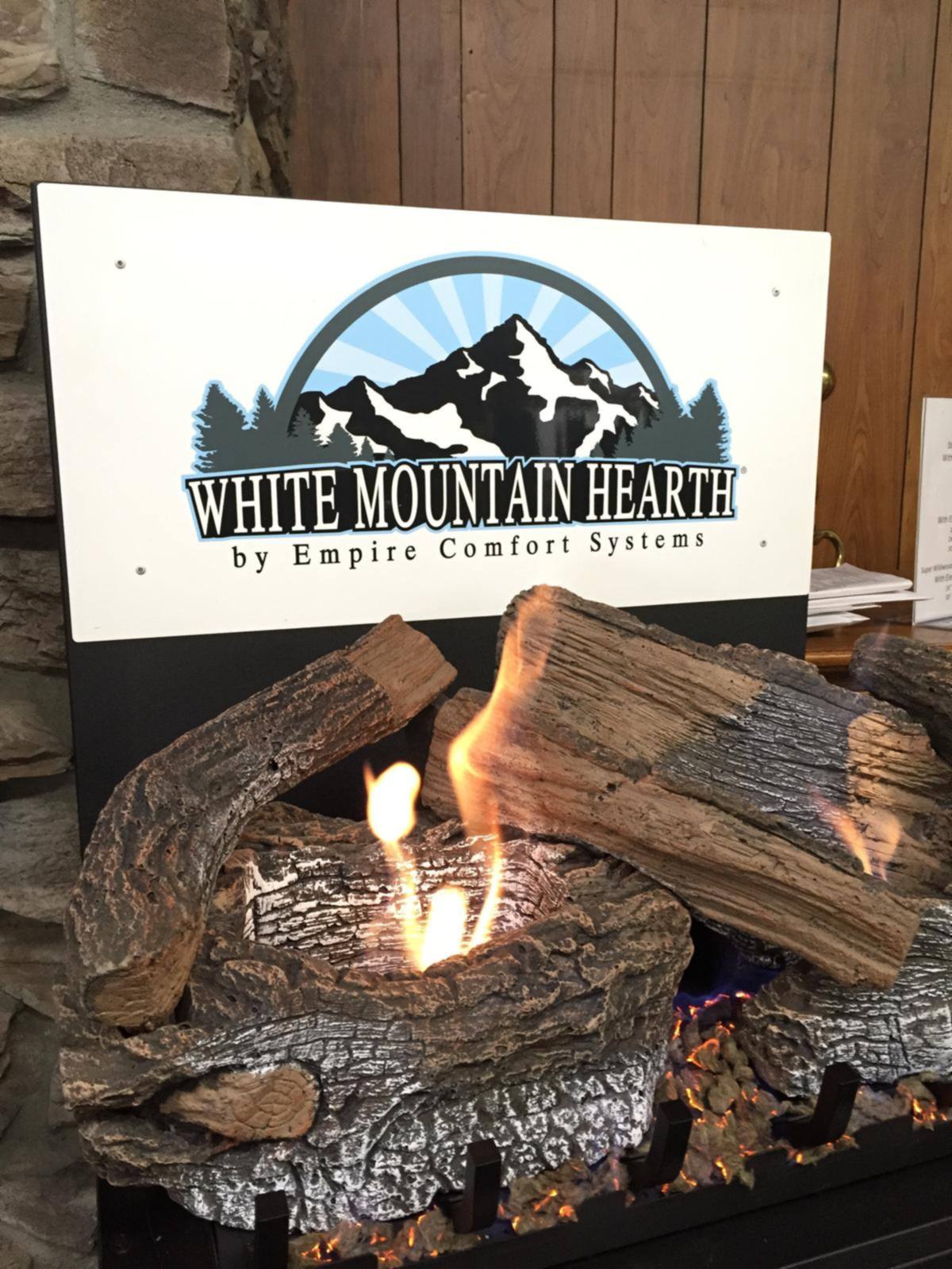 A burning gas log set below a White Mountain Hearth dealer sign