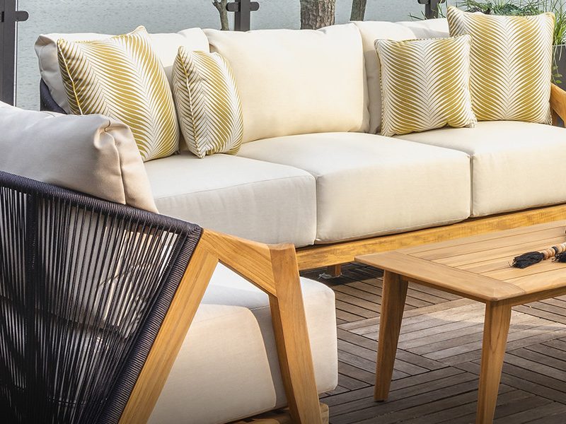 A Lloyd Flanders sofa with cream cushions and a woven chair on a lakeside deck
