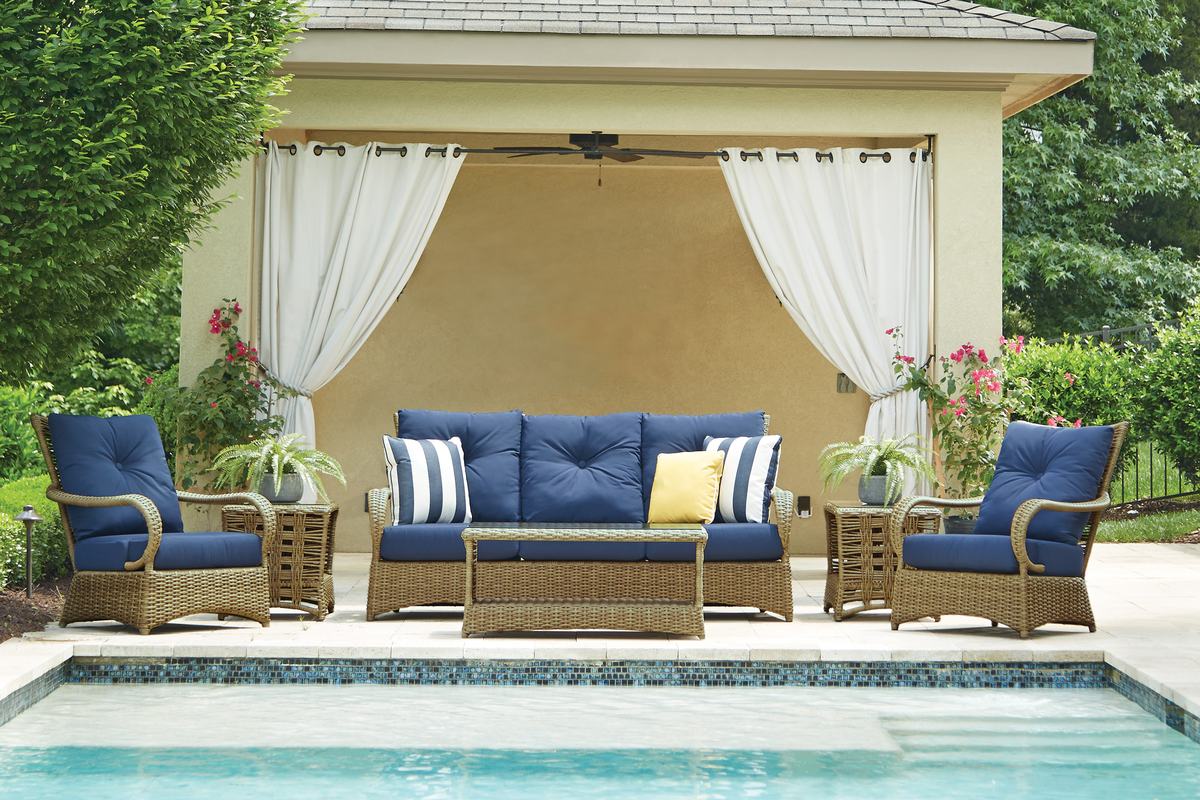 A Lloyd Flanders Magnolia wicker sofa and two lounge chairs with navy cushions beside a pool