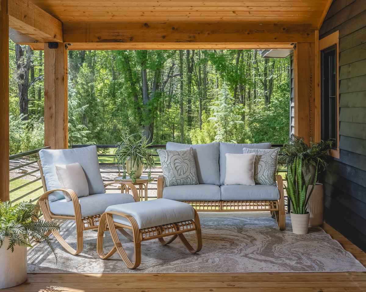 A Lloyd Flanders Riviera loveseat, lounge chair and ottoman with light blue cushions on a covered porch facing the woods