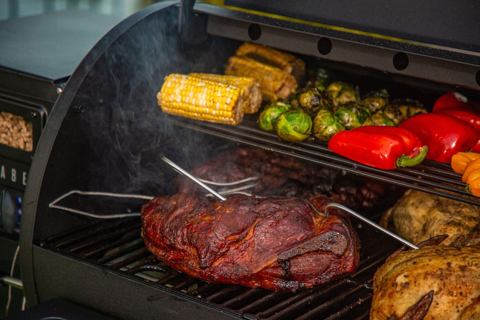 A Louisiana Grills pellet grill loaded with smoked barbecue, corn and vegetables