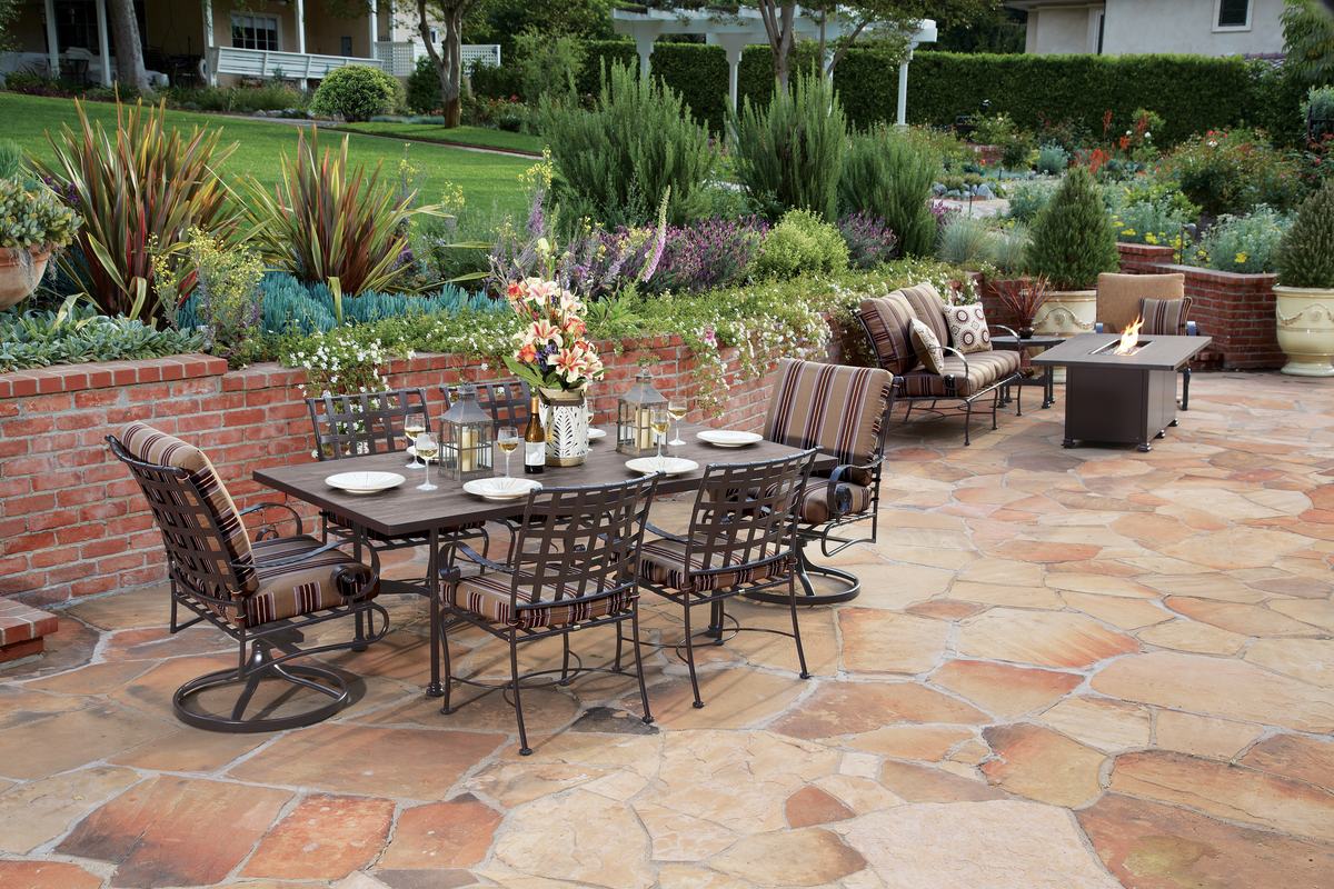 An OW Lee Classico dining set with striped cushions on a flagstone patio, with a sofa and a lit fire table behind it