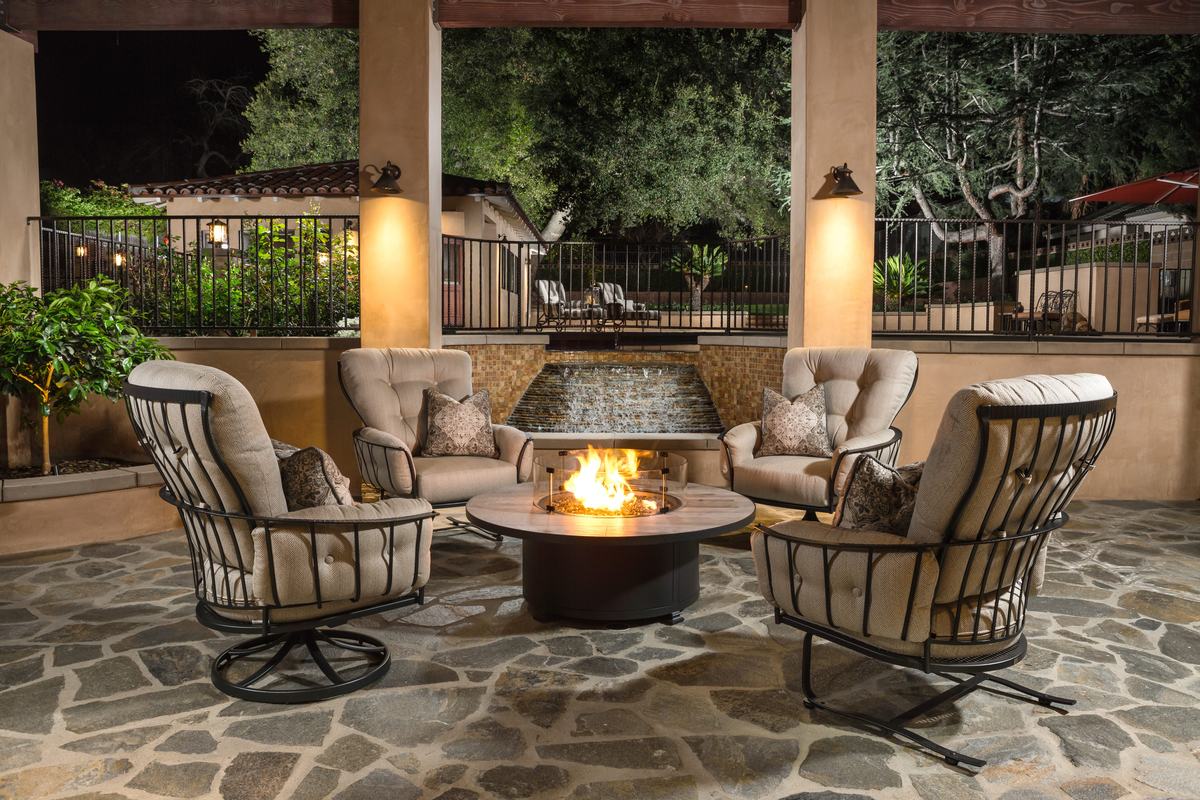 Four OW Lee Monterra lounge chairs around a lit round fire table on a stone patio in the evening