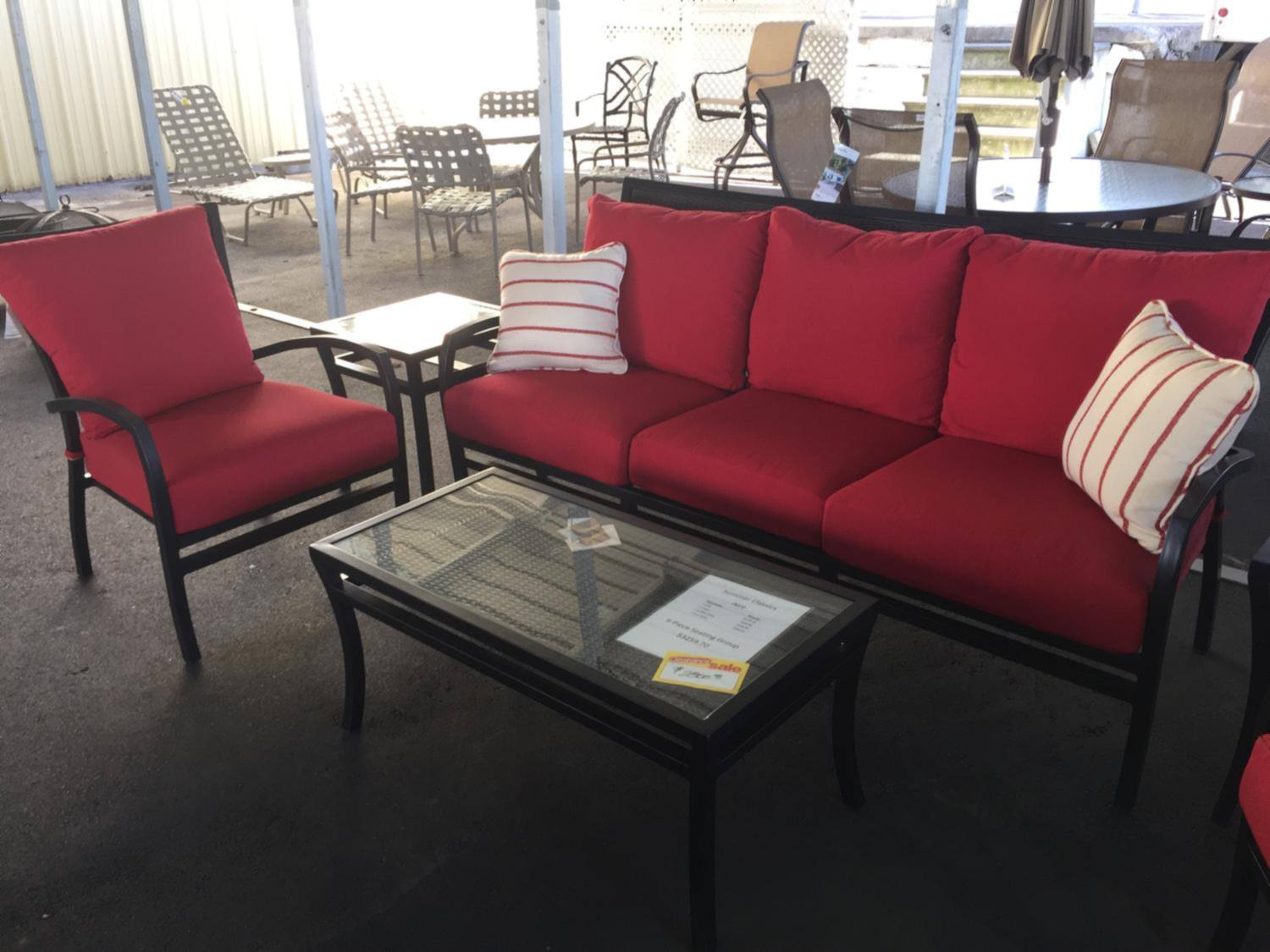 A patio sofa and chairs with red cushions and a glass coffee table in our furniture showroom