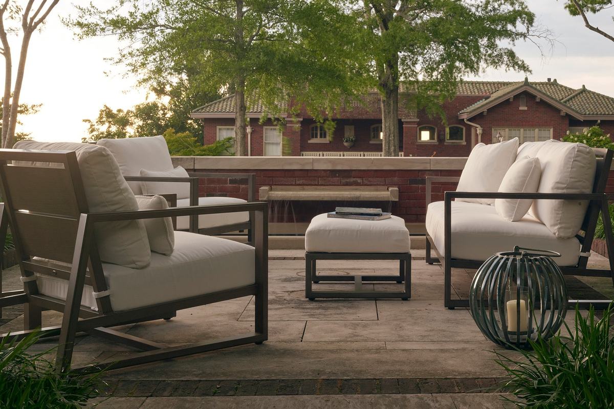Summer Classics Avondale lounge chairs and a loveseat with white cushions on a stone terrace in front of a brick house