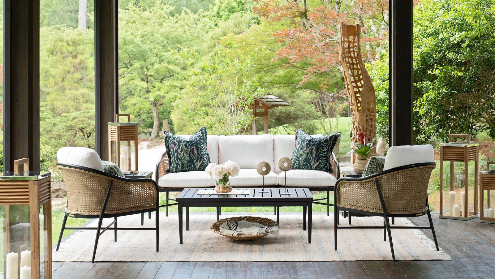 A Summer Classics Havana sofa and two cane lounge chairs on an open porch overlooking a garden
