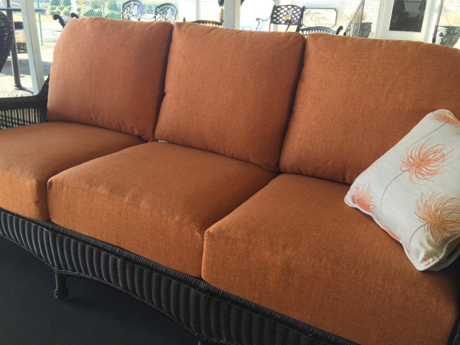 An all-weather wicker sofa with rust colored cushions