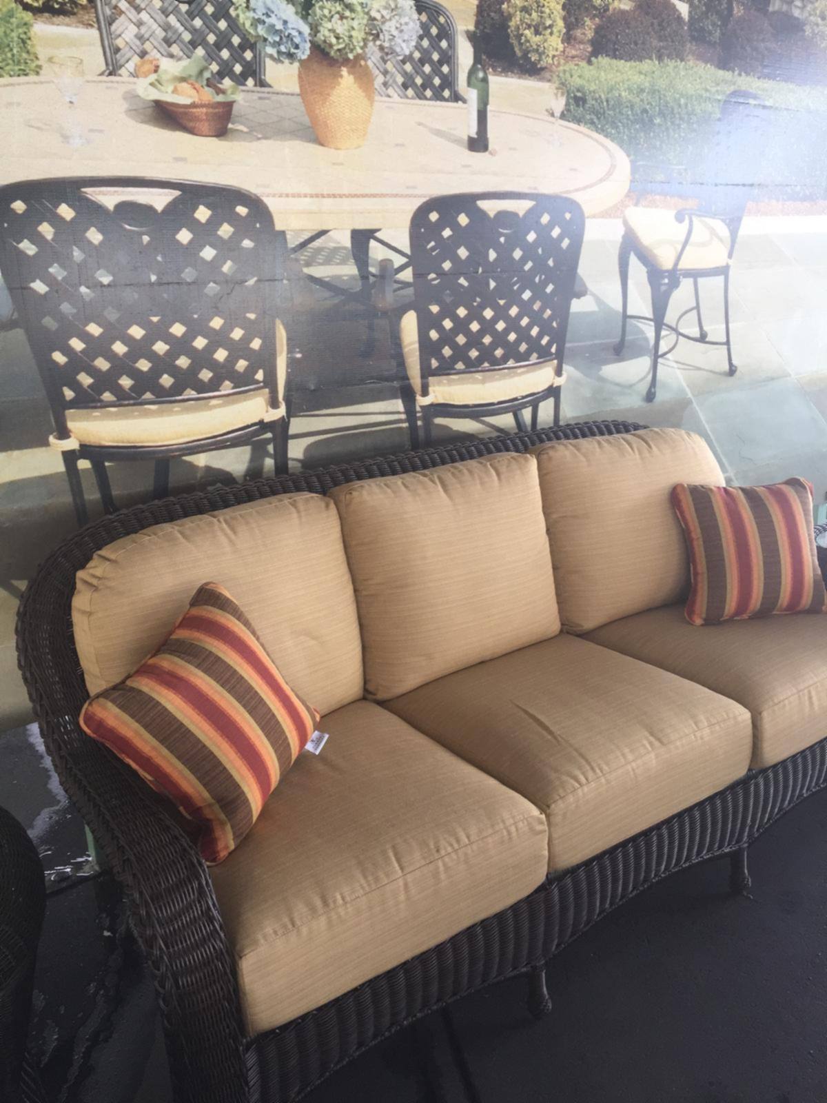 An all-weather wicker sofa with tan cushions and a striped pillow on a patio setting