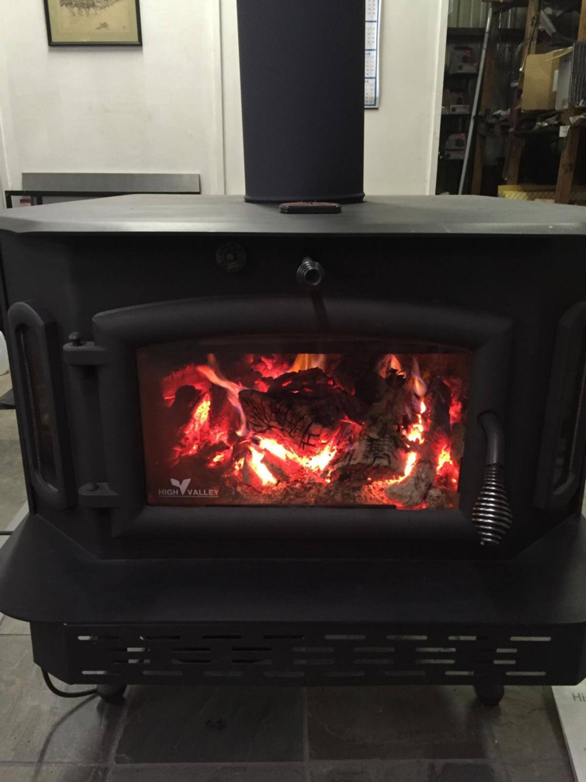 A black freestanding wood stove with a fire burning behind the glass on our showroom floor